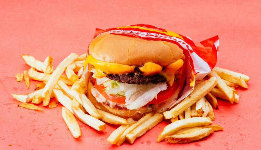 Tasty cheeseburger with fresh ingredients and french fries on a vibrant red background.